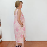 Woman wearing a pink floral dress standing against a white wall.