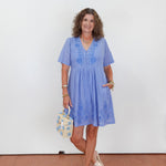 Woman in a blue dress holding a patterned handbag against a white wall.