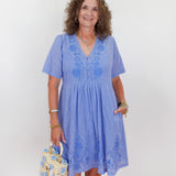 Woman wearing a blue dress with floral patterns, holding a matching handbag against a white background.