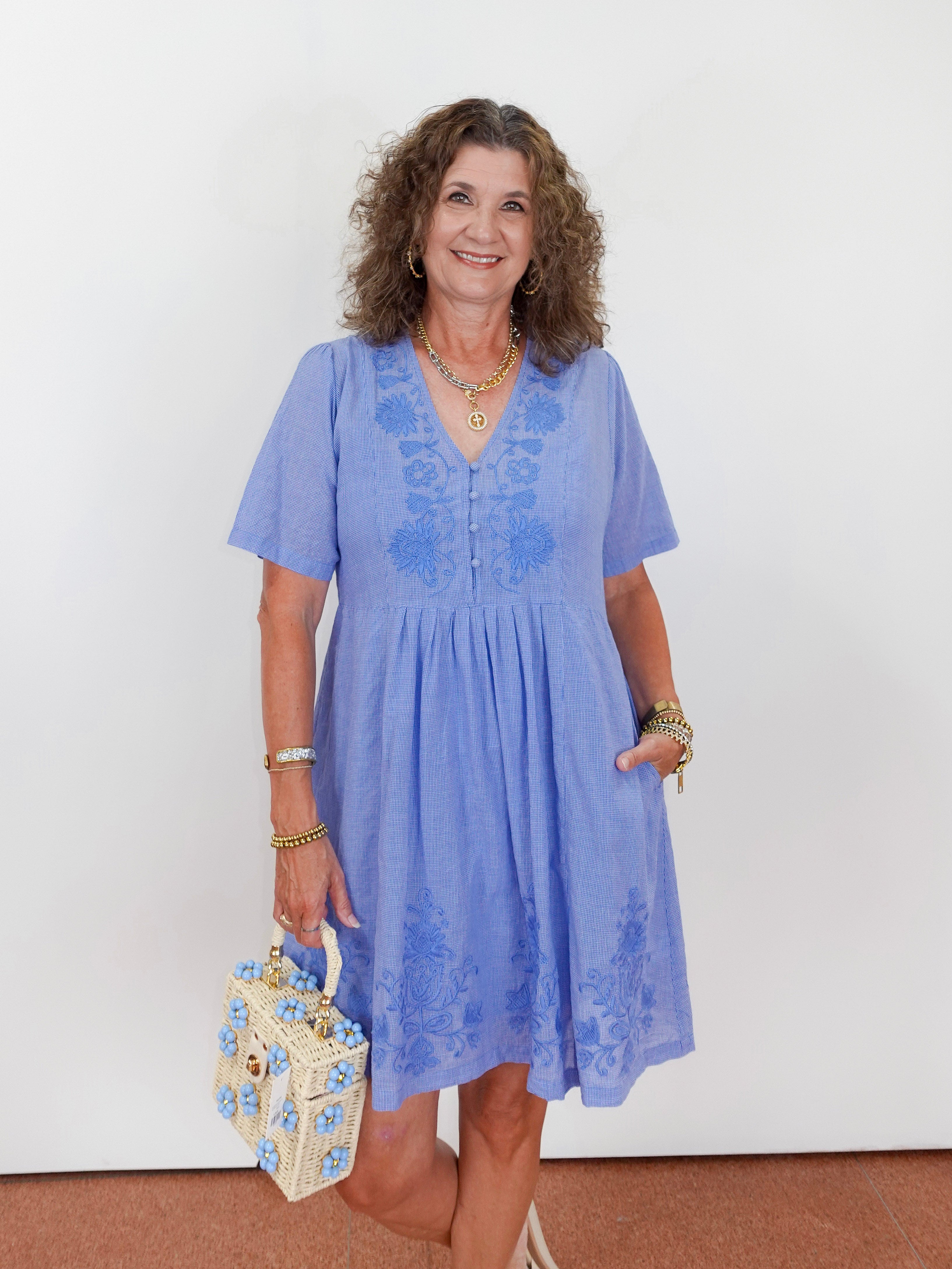 Woman wearing a blue dress with floral patterns, holding a matching handbag against a white background.