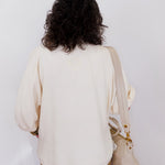 Person wearing a cream-colored sweater and holding a beige handbag against a white background