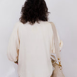 Person wearing a cream-colored sweater and holding a beige handbag against a white background