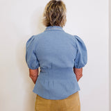 Person wearing a blue denim shirt with puffed sleeves against a white background