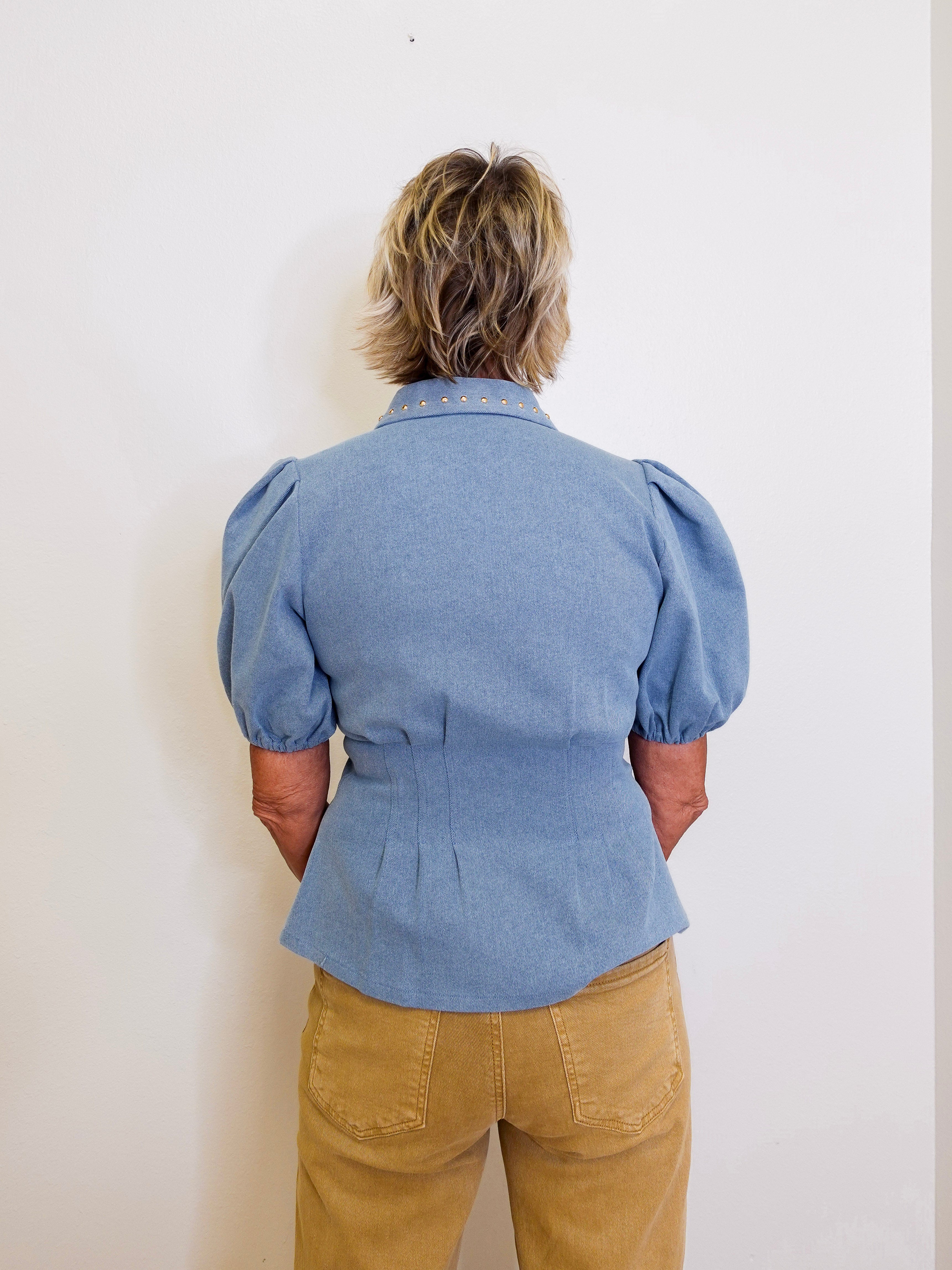 Person wearing a blue denim shirt with puffed sleeves against a white background