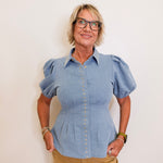 Woman wearing a blue denim shirt with puffed sleeves against a white background