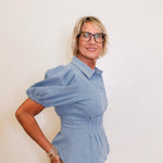 Woman wearing a blue peplum top and beige pants against a white background