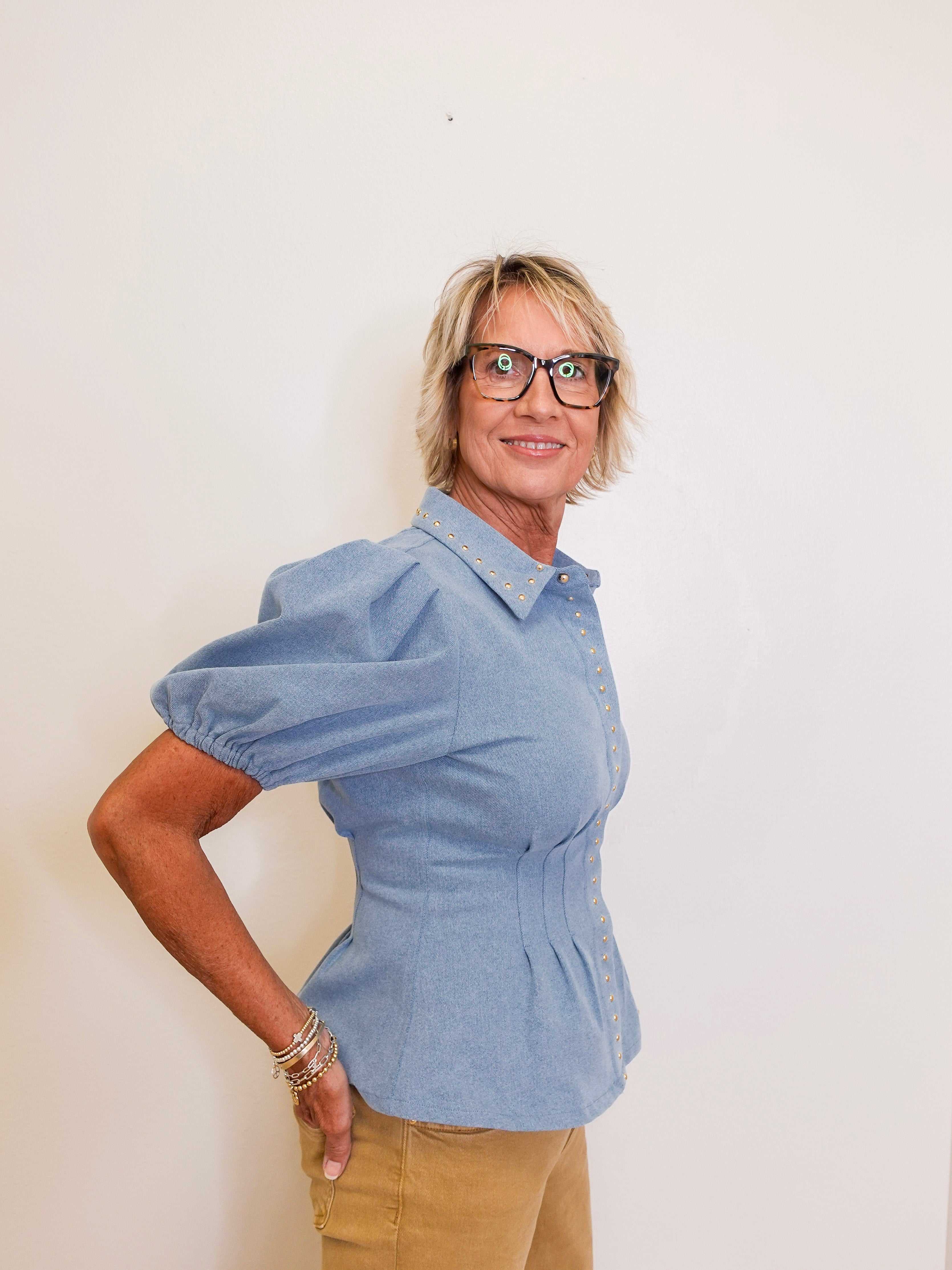 Woman wearing a blue peplum top and beige pants against a white background