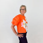 Person wearing an orange top with a floral design against a white background