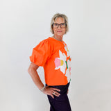 Person wearing an orange top with a floral design against a white background