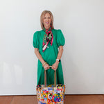 Woman in a green dress holding a colorful bag against a white wall