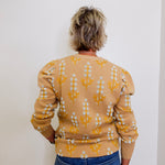 Person wearing a beige sweater with a pattern, standing against a white wall.