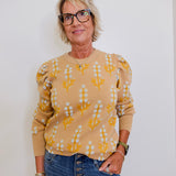 Woman wearing a yellow patterned sweater and blue jeans against a white background