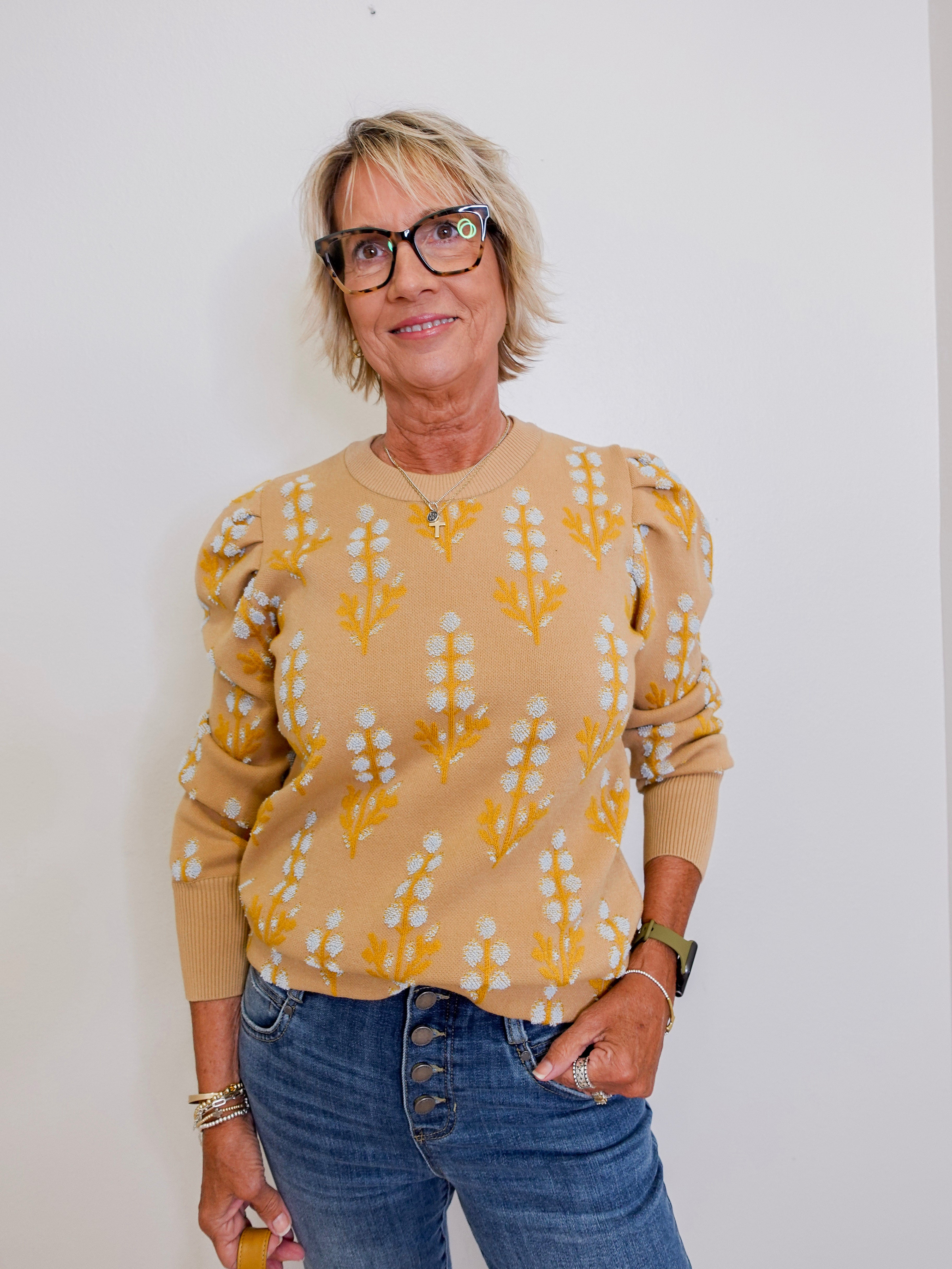 Woman wearing a yellow patterned sweater and blue jeans against a white background
