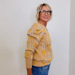 Woman wearing a yellow floral sweater and blue jeans against a white wall