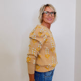 Woman wearing a yellow floral sweater and blue jeans against a white wall