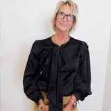 Woman wearing a black blouse with puffed sleeves against a white wall