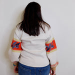 Person wearing a white sweater with colorful arm designs against a plain background