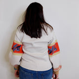 Person wearing a white sweater with colorful arm designs against a plain background