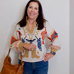 Woman wearing a colorful sweater with animal prints, holding a brown bag against a plain background