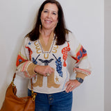 Woman wearing a colorful sweater with animal prints, holding a brown bag against a plain background