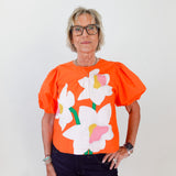 Person wearing an orange blouse with floral designs against a white background