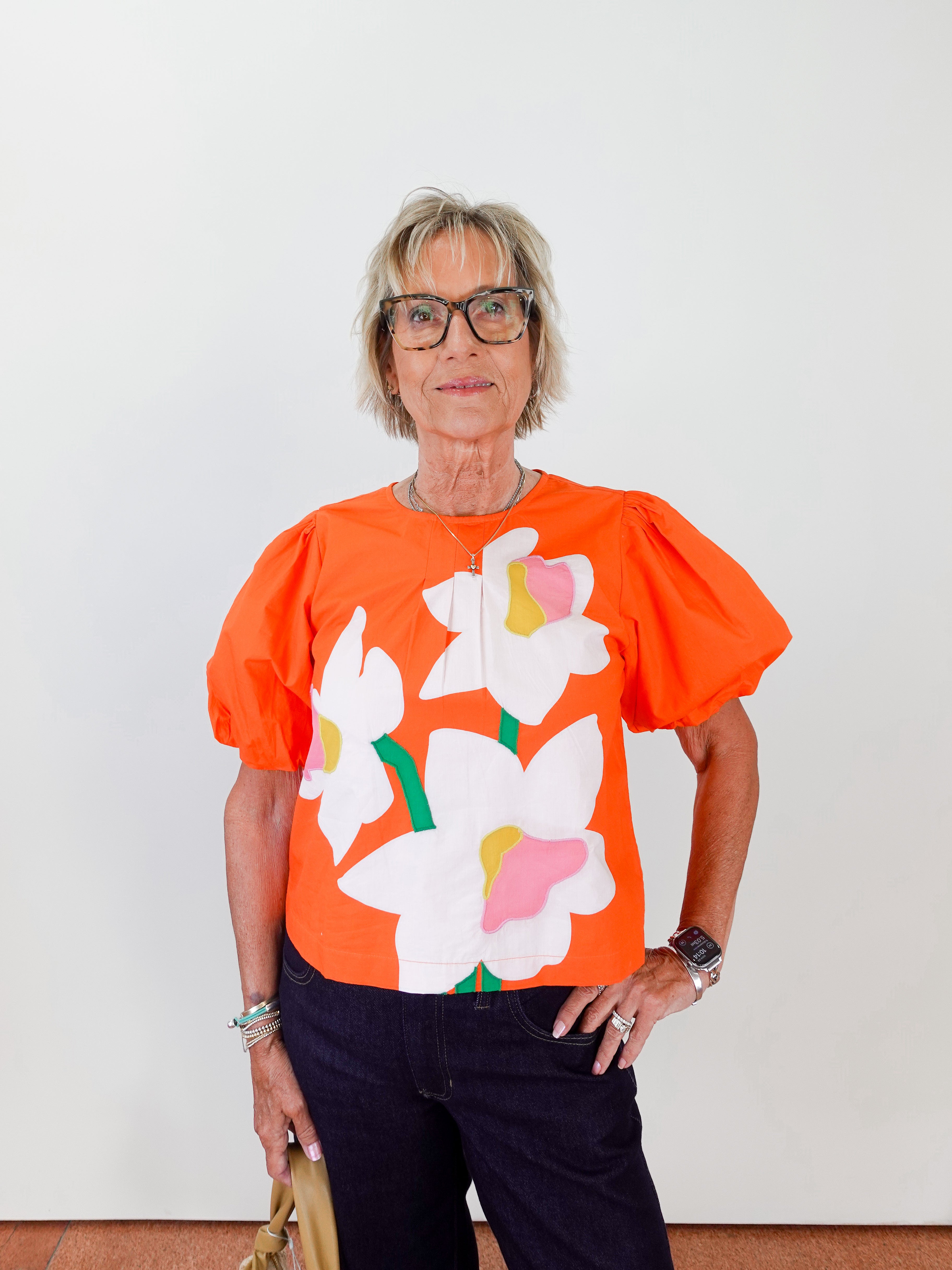 Person wearing an orange blouse with floral designs against a white background