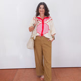 Woman wearing a floral blouse and beige pants standing against a white wall.