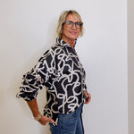 Woman wearing a black and white patterned blouse against a plain background
