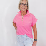 Woman wearing a pink short-sleeve top and light blue jeans against a white background