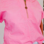 Person wearing a pink short-sleeve jacket with a gold zipper.