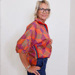 Woman wearing a colorful patterned shirt and glasses against a white wall