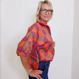 Woman wearing a colorful patterned shirt and glasses against a white wall