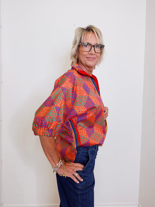 Woman wearing a colorful patterned shirt and glasses against a white wall