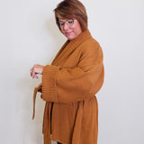 Woman wearing a brown coat against a white wall