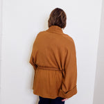 Person wearing a brown sweater against a white wall