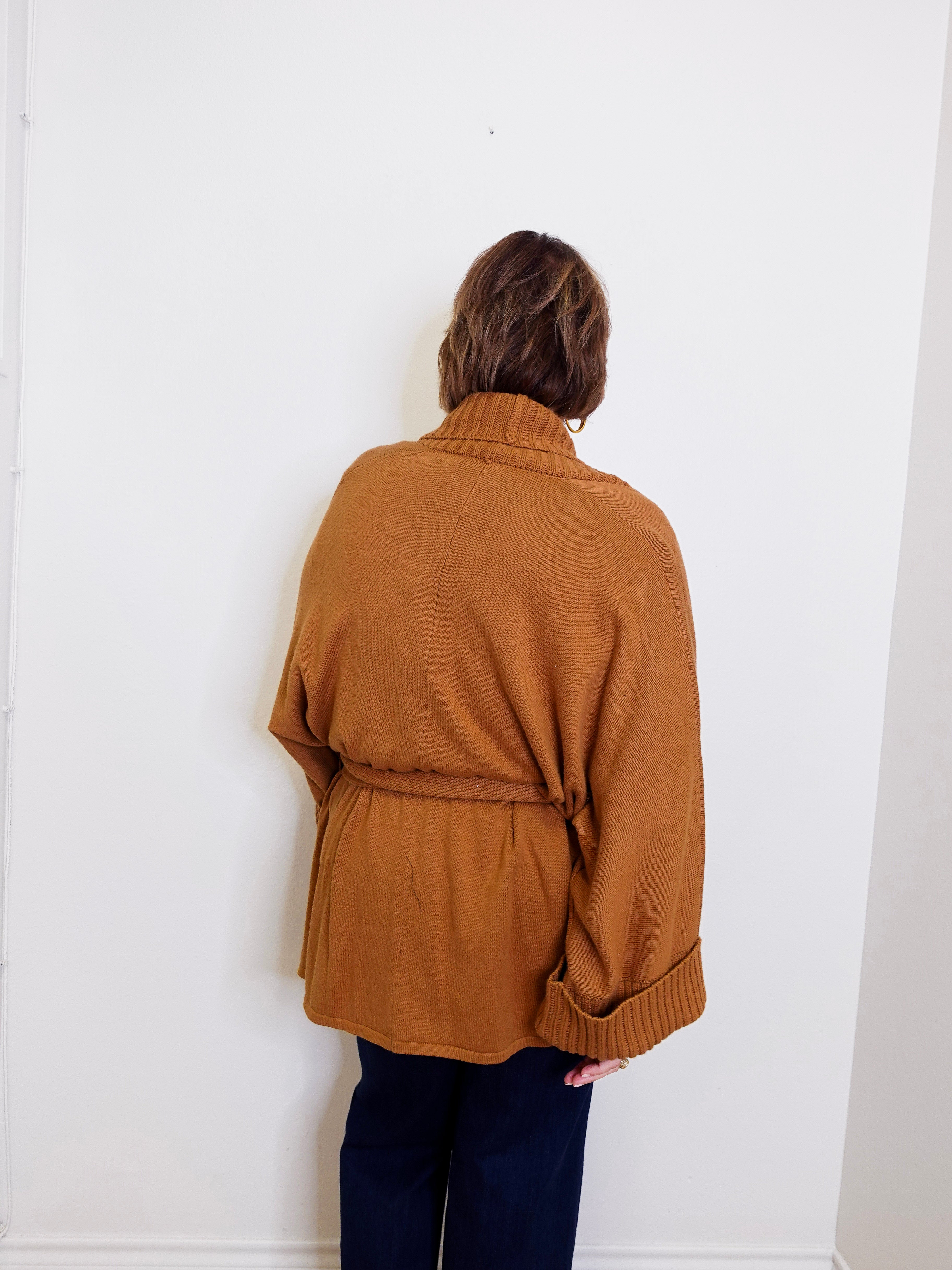 Person wearing a brown sweater against a white wall