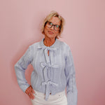 Woman wearing a light blue knitted sweater with a bow tie against a pink background