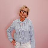 Woman wearing a light blue knitted sweater with a bow tie against a pink background