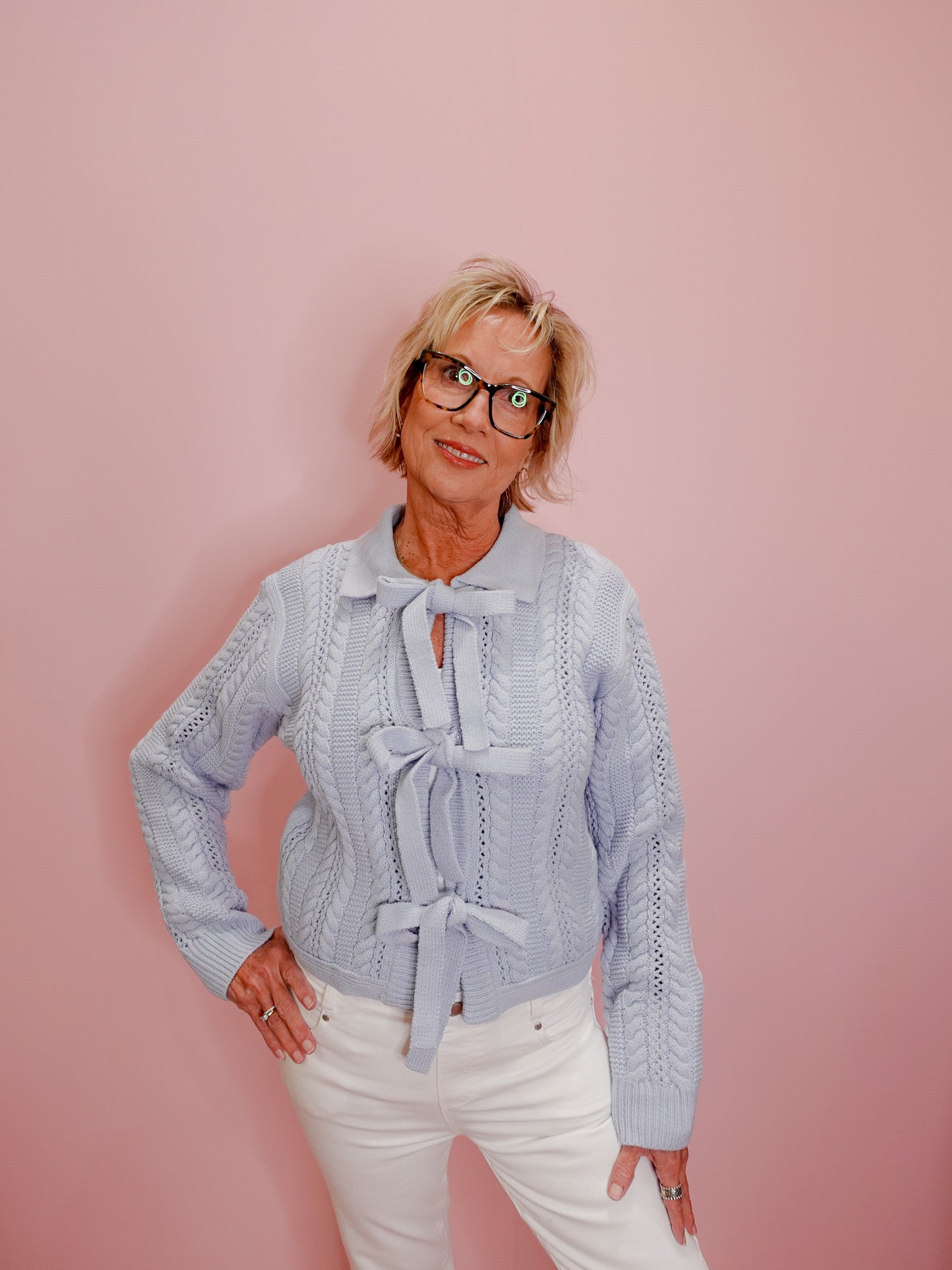 Woman wearing a light blue knitted sweater with a bow tie against a pink background
