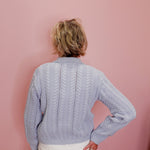 Person wearing a light blue cable knit sweater against a pink background