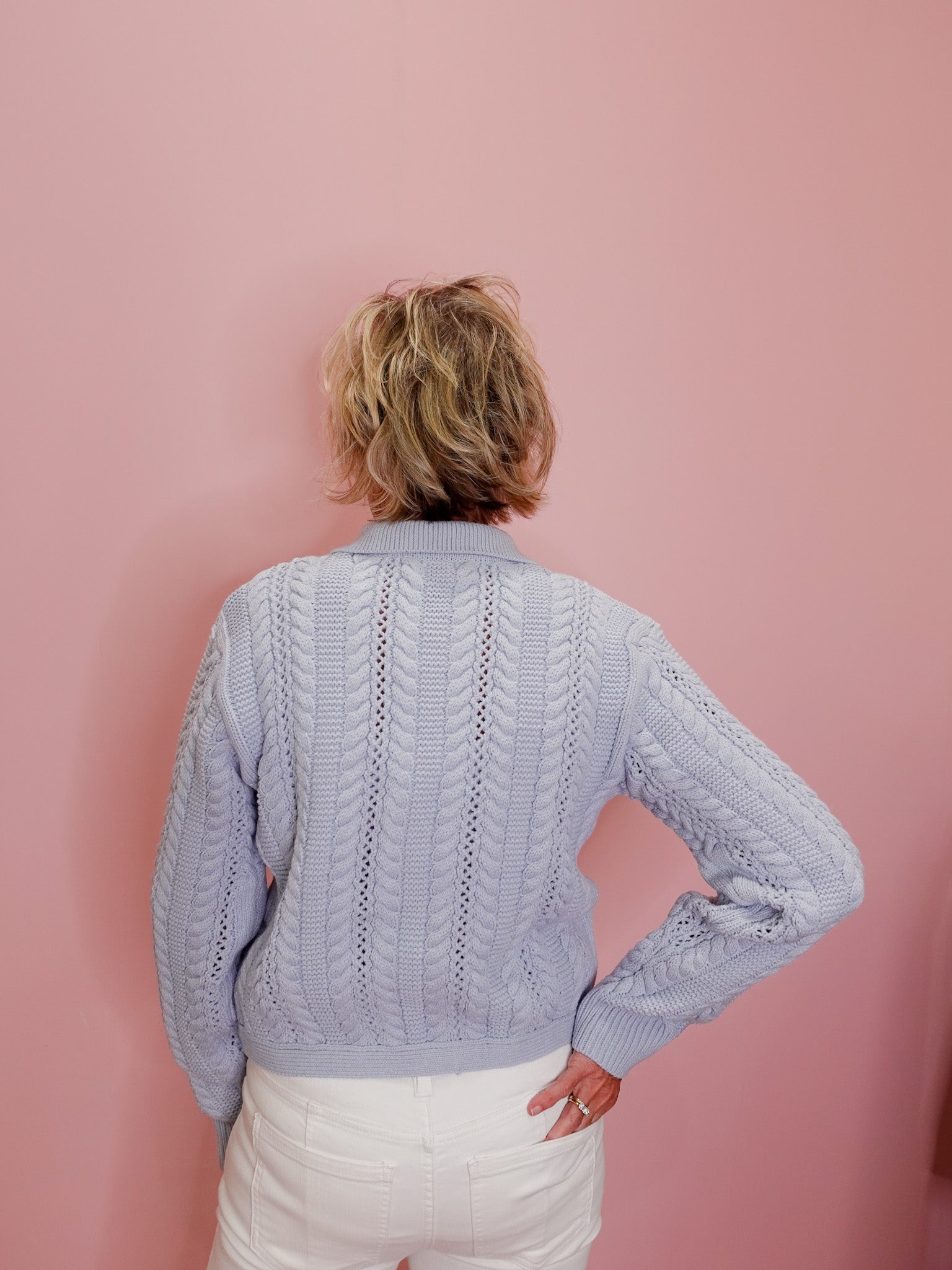 Person wearing a light blue cable knit sweater against a pink background