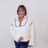 Person wearing a cream sweater with colorful trim against a white background