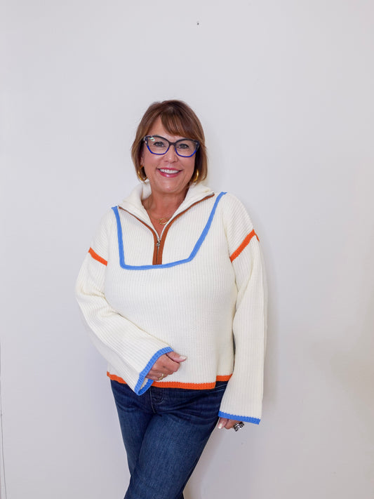 Person wearing a cream sweater with colorful trim against a white background