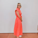 Woman wearing a bright orange dress with white stripes against a plain background