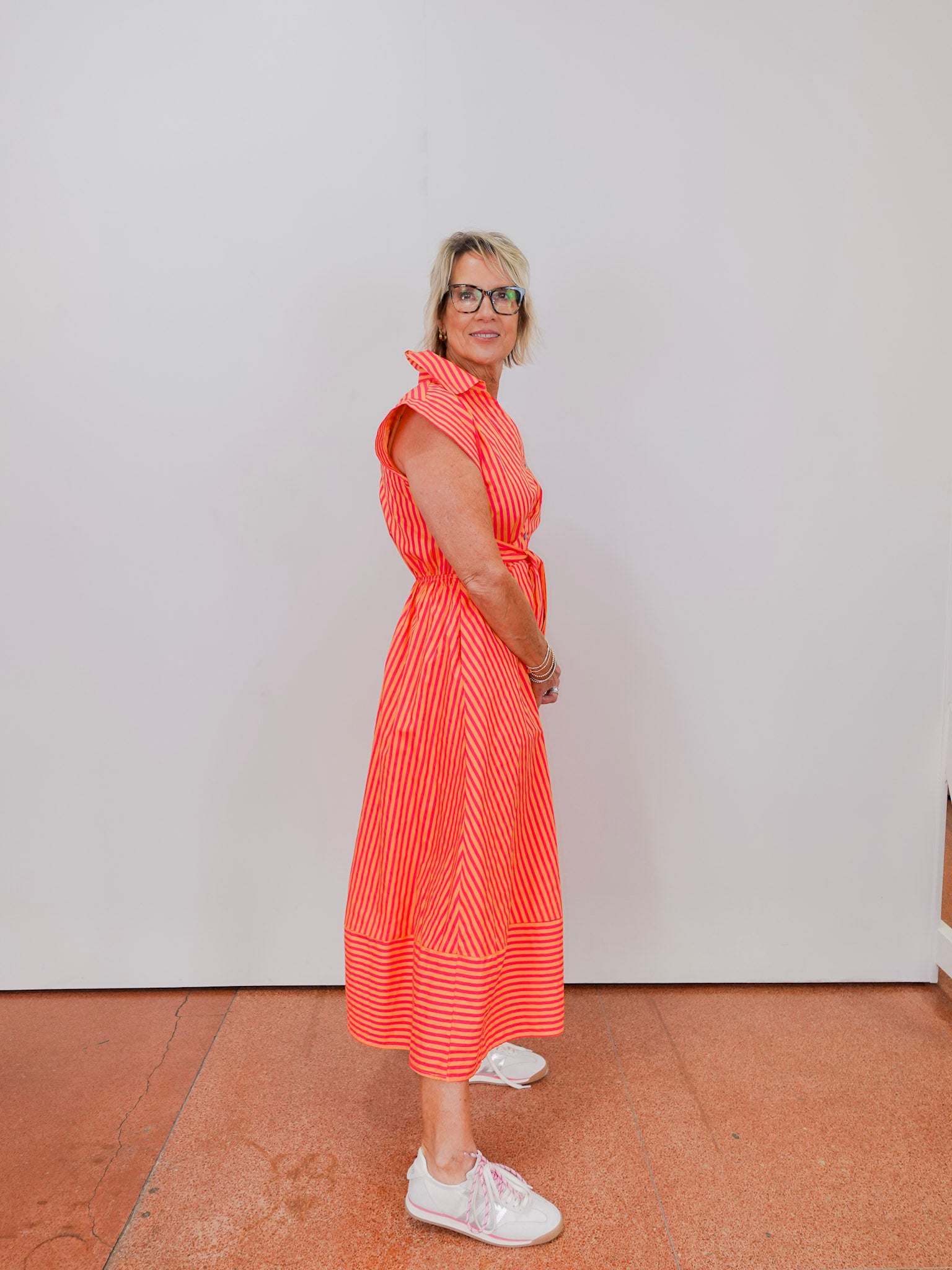 Woman wearing a bright orange dress with white stripes against a plain background