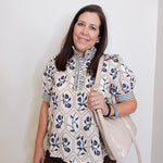 Woman wearing a patterned blouse holding a beige handbag against a white background