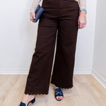 Person wearing brown wide-leg pants with a colorful top and blue sandals on a light wooden floor.