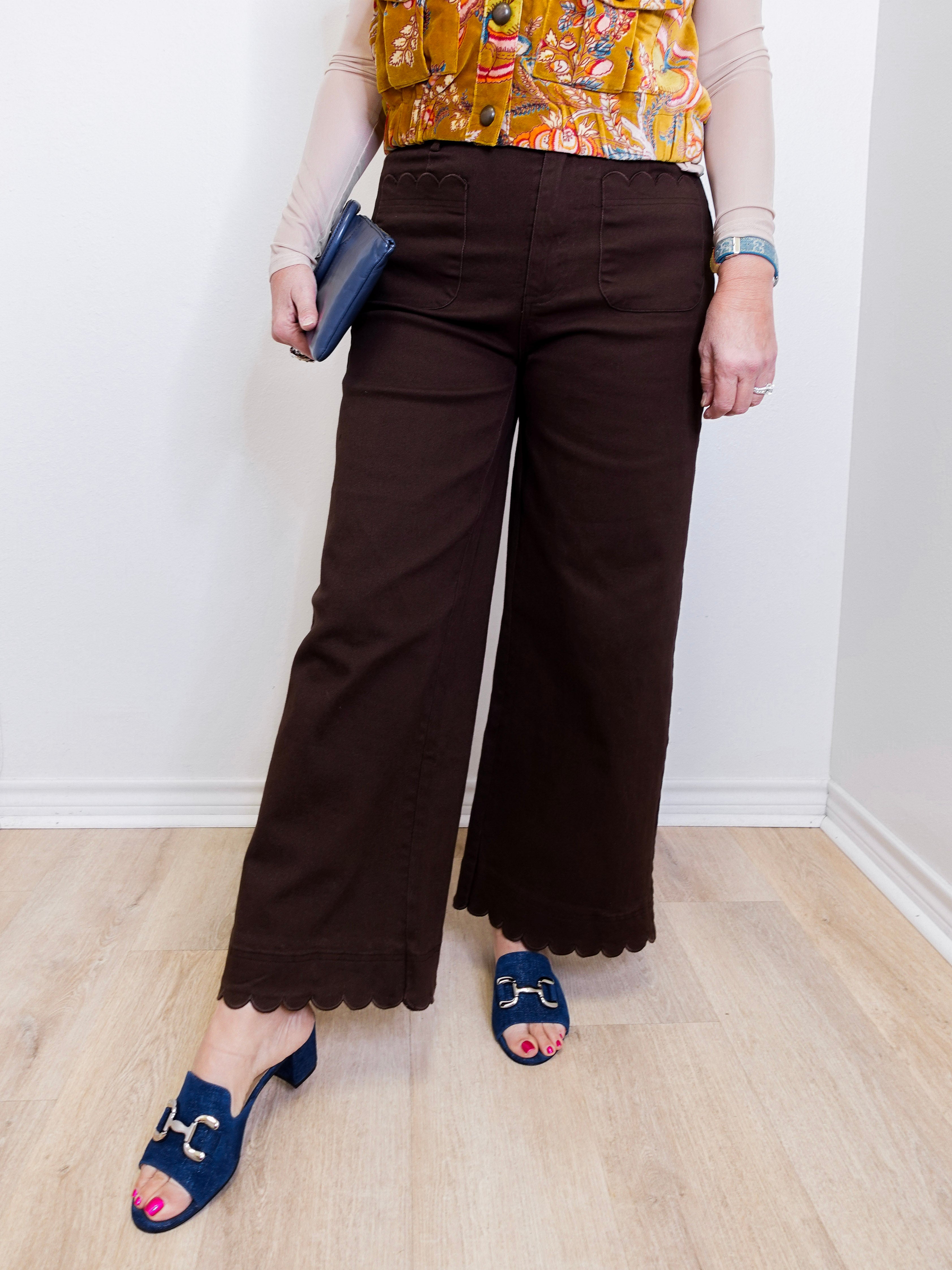 Person wearing brown wide-leg pants with a colorful top and blue sandals on a light wooden floor.