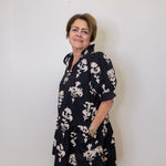 Woman wearing a black floral dress against a white wall