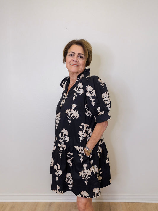 Woman wearing a black floral dress against a white wall